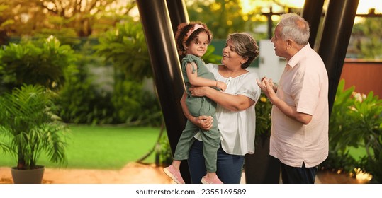 Happy Indian old grandmother standing holding cute little child girl in arms hands playing together outdoor home. Beautiful senior couple talking with small adorable daughter enjoying summer holiday - Powered by Shutterstock