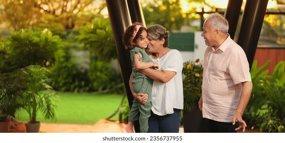 Happy Indian old grandmother standing holding cute little child girl in arms hands playing together outdoor home. Beautiful senior couple talking with small adorable daughter enjoying summer holiday - Powered by Shutterstock