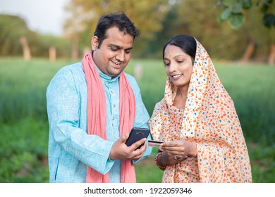 Happy indian rural farmer couple using smartphone to make online payment with debit card in agricultural field, shopping on internet with cellphone secure banking service system concept.