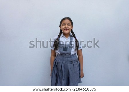 Happy Indian school girl standing against white wall