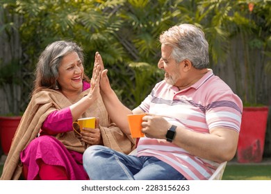 Happy indian senior couple drinking tea or coffee in colorful mugs sitting at garden. - Powered by Shutterstock