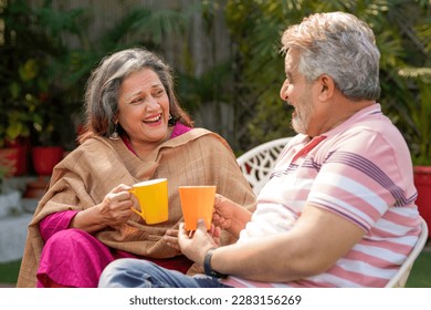 Happy indian senior couple drinking tea or coffee in colorful mugs sitting at garden. - Powered by Shutterstock