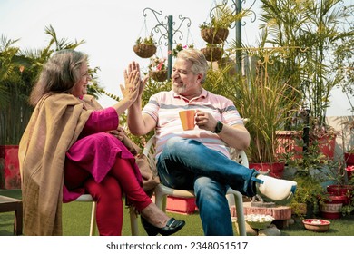 Happy indian senior couple drinking tea or coffee in colorful mugs sitting at garden. - Powered by Shutterstock