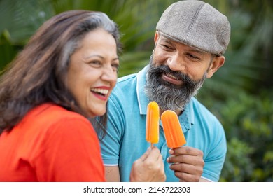 Happy Indian Senior Couple Eating Ice Lolly Or Ice Cream In A Park Outdoor, Old Mature People Enjoy Retirement Life. Summer Holidays. Selective Focus.