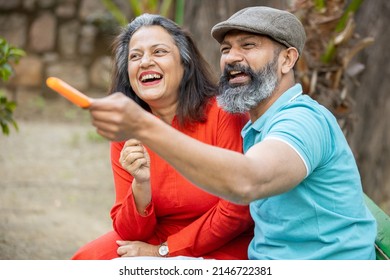 Happy Indian Senior Couple Eating Ice Lolly Or Ice Cream In A Park Outdoor, Old Mature People Enjoy Retirement Life. Summer Holidays. Selective Focus.