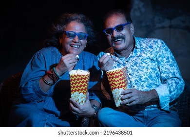 Happy indian senior couple wearing 3d glasses eating popcorn and laughing while sitting and watching movie at the cinema. - Powered by Shutterstock