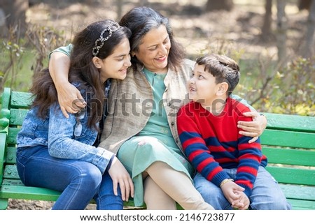Happy indian senior grandmother sitting with her grandchildren outdoor together, smiling mature 60s asian granny with her grand son and daughter at park. Old lady spend time have fun with kids.