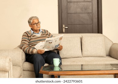 Happy Indian Senior man in glasses drinking coffee and reading newspaper at home. - Powered by Shutterstock