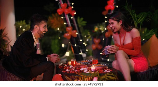 Happy Indian smiling two surprised couple sitting on chair dating outdoor home. Handsome boyfriend gives gift to girlfriend celebrate Valentine's Day spend time enjoying holiday weekend together  - Powered by Shutterstock