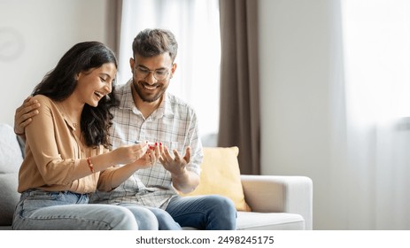 Happy indian spouses holding positive pregnancy test, sitting on couch at home together, couple celebrating awaiting baby, copy space - Powered by Shutterstock