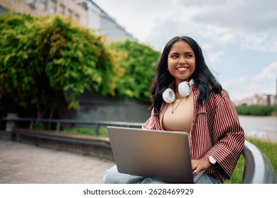Happy Indian student e-learning over her laptop at campus and looking away. Copy space. 