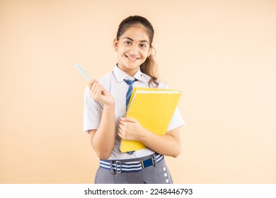 Happy Indian student schoolgirl wearing school uniform holding books and bag standing isolated over beige background, Studio shot,closeup, Education concept. - Powered by Shutterstock