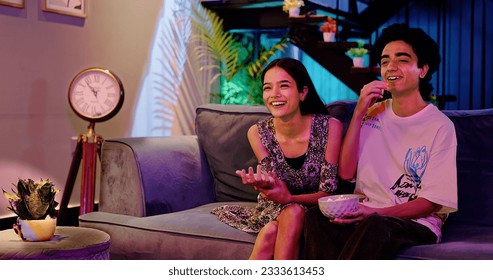 Happy Indian teenager couple sitting on cozy sofa watching favourite movie TV having fun enjoy laughing weekend together. Smilling teen boyfriend girl friend hold popcorn bowl eating snack at home - Powered by Shutterstock