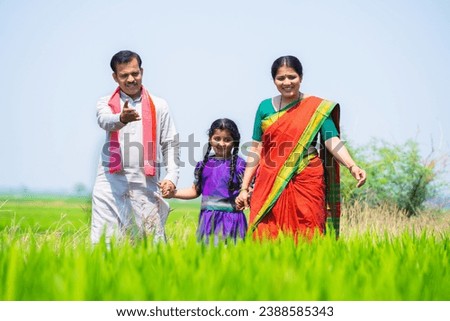 Happy indian village couple with kid walking by talking each other near paddy field - concept of sustainable lifestyle, family bonding and rural India.