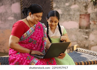 Happy Indian village family of single mother and daughter sitting using the laptop sitting outside the house - Powered by Shutterstock