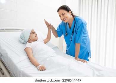 Happy indian woman nurse or medical staff give a high five to little girl cancer patient lying on hospital bed undergoing course of chemotherapy. - Powered by Shutterstock