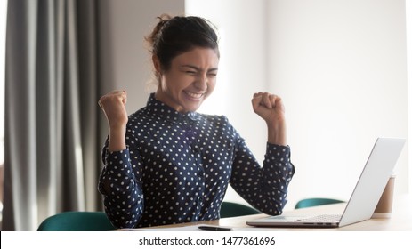 Happy indian woman office worker feeling excitement raising fists celebrates career ladder promotion or reward, businesswoman sitting at desk receive online news, great results successful work concept - Shutterstock ID 1477361696
