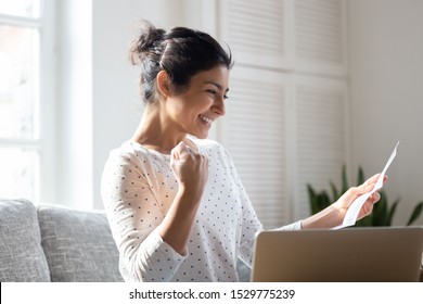 Happy Indian Woman Reading Good News In Letter, Notification, Holding Paper, Smiling Girl Rejoicing Success, Student Excited By Positive Exam Results, Showing Yes Gesture, Sitting On Couch At Home