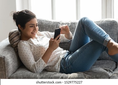 Happy Indian Woman Relaxing On Couch At Home, Using Phone Close Up, Smiling Girl Browsing Mobile Device Apps, Chatting Online With Friends In Social Network, Looking At Cellphone Screen, Having Fun