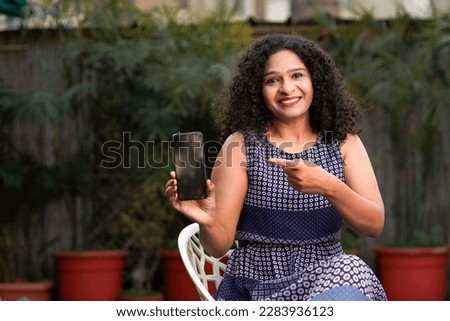 Happy Indian woman showing smartphone empty screen.