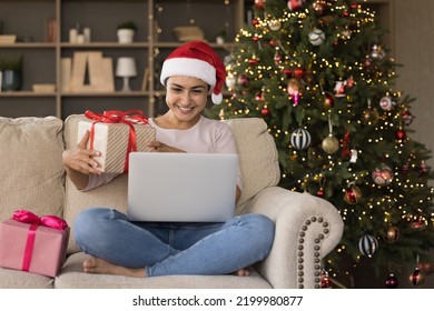 Happy Indian Xmas girl making video call from home, using laptop computer on couch at Christmas tree, holding gift box, thanking for present. Young woman, blogger recording festive New Year post - Powered by Shutterstock