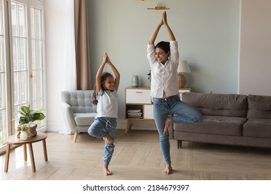 Happy Indian yogi mom teaching daughter kid to do yoga at home, standing in tree pose, smiling, laughing, talking, enjoying home exercises, leisure activities, keeping healthy life style - Powered by Shutterstock