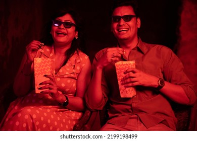 Happy Indian Young Couple Wearing 3d Glasses Eating Popcorn And Laughing While Sitting And Watching Movie At The Cinema.