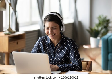 Happy indian young girl student wear headphone watch webinar listen online course communicate by conference video call e learn language in app laugh study with teacher lesson look at laptop at home - Shutterstock ID 1606120012