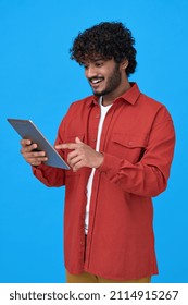 Happy Indian Young Man Using Digital Tablet Isolated On Blue Background. Smiling Ethnic Hipster Guy Holding Pad Playing Game In App, Buying Online In Ecommerce Store, Reading Ebook. Vertical