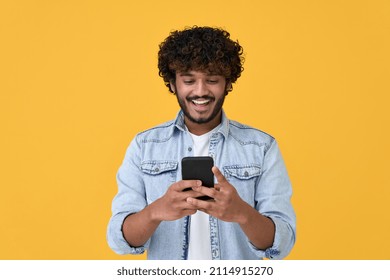 Happy indian young man using cell phone isolated on yellow background. Smiling ethnic hipster guy holding smartphone playing game in app, dating online, buying online in e commerce store on cellphone. - Powered by Shutterstock