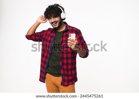 Happy Indian young music lover listening to favorite audio track music band in headphones isolated over white background. Hindi man dancing to the beat