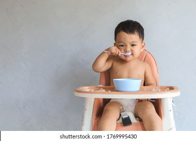 Happy infant Asian baby boy eating food by himself on baby high chair and making mess with copy space. - Shutterstock ID 1769995430