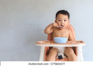 Happy infant Asian baby boy eating food by himself on baby high chair and making mess with copy space. - Shutterstock ID 1770601577
