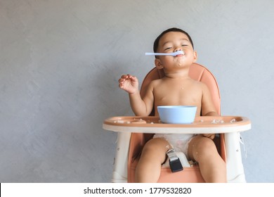 Happy infant Asian baby boy eating food by himself on baby high chair and making mess with copy space. - Shutterstock ID 1779532820
