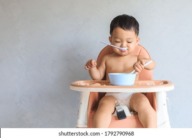 Happy Infant Asian Baby Boy Eating Food By Himself On Baby High Chair And Making Mess With Copy Space.