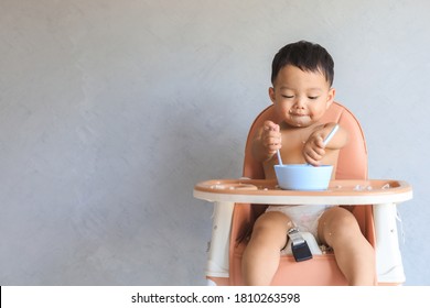 Happy infant Asian baby boy eating food by himself on baby high chair and making mess with copy space. - Shutterstock ID 1810263598