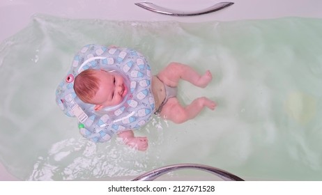 Happy Infant Baby Boy Smiling While Swimming In The Bathtub With A Rubber Ring On His Neck. Four Month Old Child, View From Above