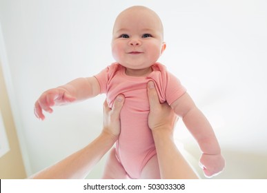 Happy infant baby girl being held up in the air by her parent