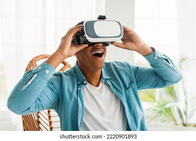 Happy Inspired Young Black Man In VR Glasses With Open Mouth Enjoy Online Virtual Reality Game In Light Living Room Interior, Close Up. Facial Expression, New App, Entertainment At Home, Covid-19