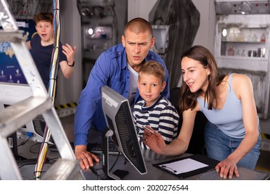 Happy Interested Family With Teen Sons Trying To Get Out Of Closed Space Of Escape Room Stylized As Abandoned Bunker, Using Computer