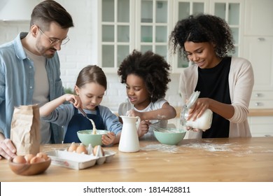 Happy interested multiethnic small children girls in aprons involved in preparing dough for homemade pastry with affectionate loving african american mommy and european father in modern kitchen. - Powered by Shutterstock