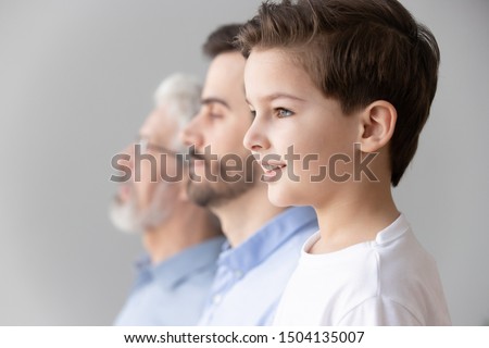 Happy intergenerational muti 3 three generation men family portrait, cute child boy son grandson looking forward think dream of future stand in row with young father and old grandfather, side view