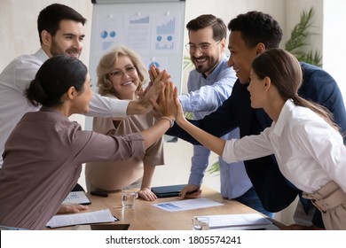 Happy International Group Of Different Generations Business People, Joining Hands Over Table In High Five Gesture, Celebrating Common Corporate Success Or Involved In Motivating Team Building Activity