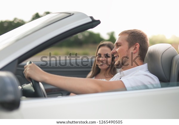 Happy International Women\'s Day at 8 March,\
Young couple has a vacation driving a white cabriolet with opened\
roof. Happy beautiful girl and handsome man are smiling. Concept\
for your adventure