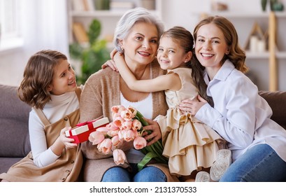 Happy International Women's Day. Smiling Multi Generational Family Grandmother, Mother And Daughter With Flowers  Cheerfully Celebrate The Spring Holiday Mother's Day At Home