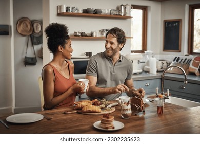 Happy interracial couple, breakfast and morning in kitchen for healthy meal, talk or bonding at home. Man and woman smiling for coffee, conversation or tea and food on weekend together by the table - Powered by Shutterstock