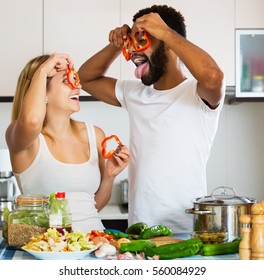 Happy interracial couple cooking vegetables and laughing in home interior - Powered by Shutterstock