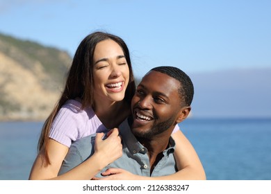 Happy interracial couple or friends laughing on piggyback on the beach - Shutterstock ID 2126383247