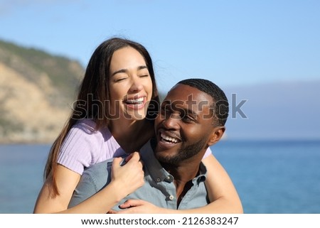 Happy interracial couple or friends laughing on piggyback on the beach