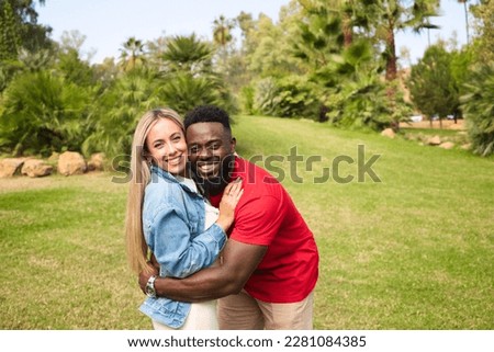 Happy interracial couple hugging in park looking at camera for photo. They are happy and excited.